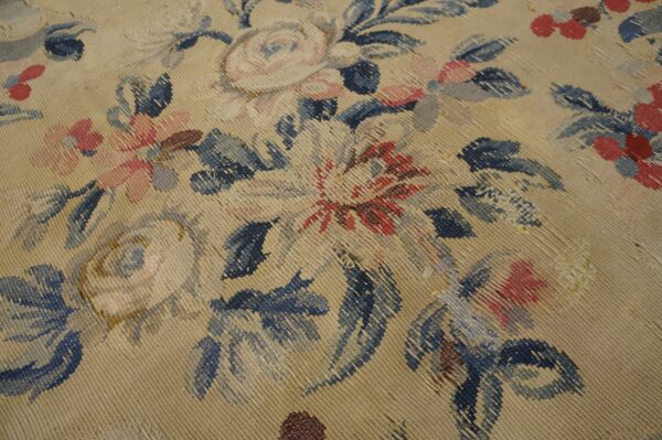 Textured close-up of a beige flat-weave rug featuring large floral designs in dusty blue, pink, and red.