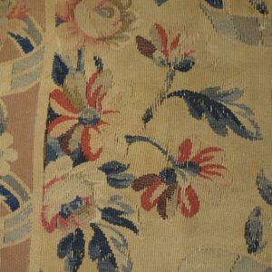 Worn flat-weave rug featuring faded blue and red floral patterns on a tan ground with a rose border.