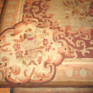 Ornate low-pile rug with large floral and scroll patterns in beige, rust, and brown rests on a wood floor.