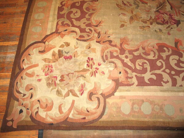 Ornate low-pile rug with large floral and scroll patterns in beige, rust, and brown rests on a wood floor.