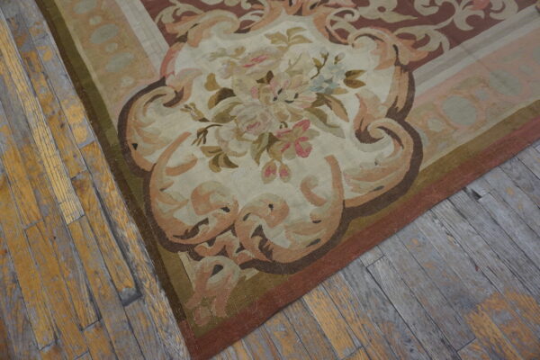 Muted low-pile rug with a detailed floral medallion and cartouche border lies on aged wood planks.