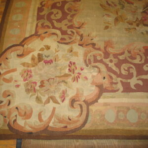 Flat weave rug displaying ornate floral and scrolling patterns in beige, rust, and pink on a hardwood floor.