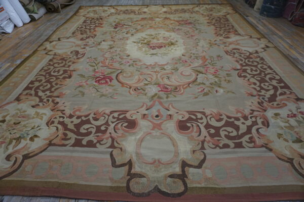 Low-pile classical rug with blush pink floral elements and ornate borders displayed on wood planks.