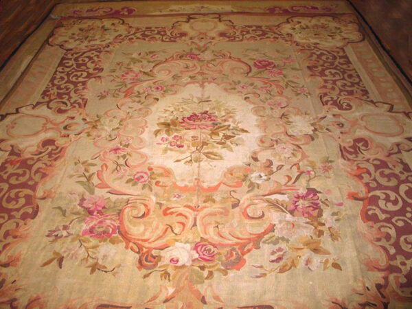 Low-pile rug with a beige ground featuring pink florals, peach scrolls, and deep red patterned borders.