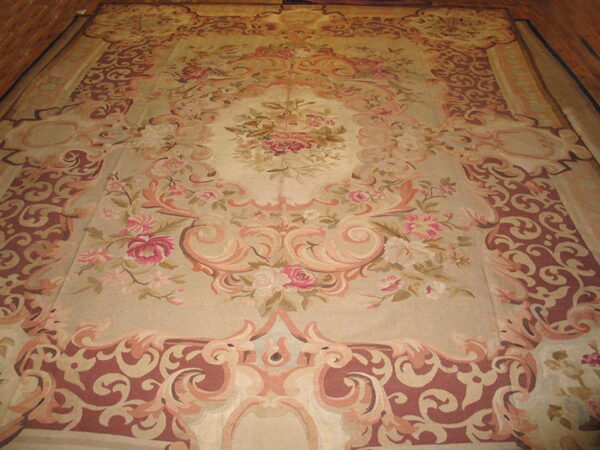Large ornate rug featuring a floral medallion and scrolls in beige, dusty rose, and deep reddish-brown.