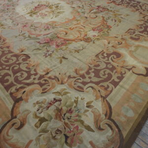 Ornate pale green and brown rug with large pink and sage floral motifs resting on distressed gray wood flooring.