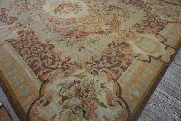 Ornate pale green and brown rug with large pink and sage floral motifs resting on distressed gray wood flooring.