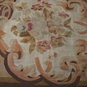 Ornate flatweave rug displaying a faded floral medallion and curving border motifs in beige, rose, and rust.