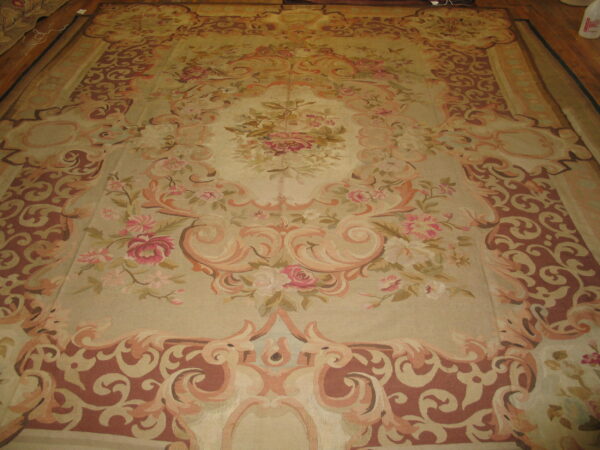 Ornate low-pile rug with a central floral medallion and dusty rose borders laid across wooden floorboards.