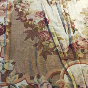 Folded low-pile rug displaying an intricate floral and scroll pattern with burgundy, olive, and tan colors.