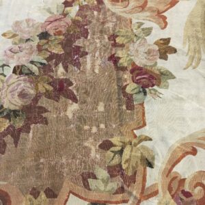 Muted floral and scroll pattern rug detail in cream, rose, and gold with a distinct ribbed texture.