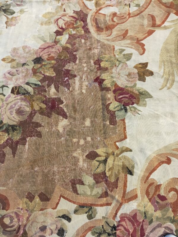 Muted floral and scroll pattern rug detail in cream, rose, and gold with a distinct ribbed texture.