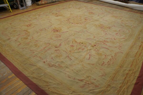 Oversized beige rug featuring an elaborate, muted pink and gold floral design laid on wood flooring.