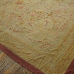 Corner of a yellow and pink ornate floral rug with a reddish border rests on distressed wood planks.