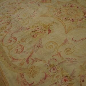 Low pile rug featuring scrolling floral patterns in faded pink and yellow tones on dark wood flooring.