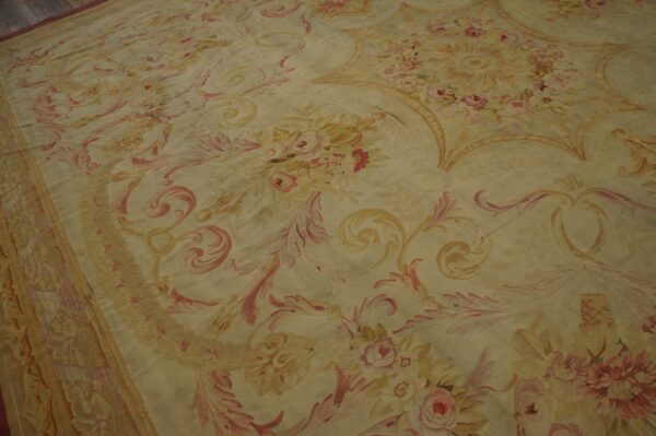 Low pile rug featuring scrolling floral patterns in faded pink and yellow tones on dark wood flooring.