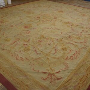 Low-pile rug with a beige field, scrolling pink floral pattern, and burgundy outer border on wood planks.
