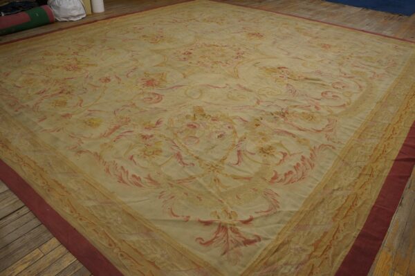 Low-pile rug with a beige field, scrolling pink floral pattern, and burgundy outer border on wood planks.
