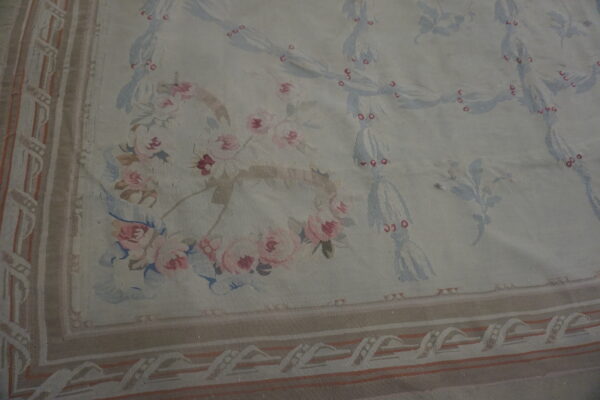 Low-pile cream rug with an ornate pale blue and pink floral trellis pattern on wood flooring.