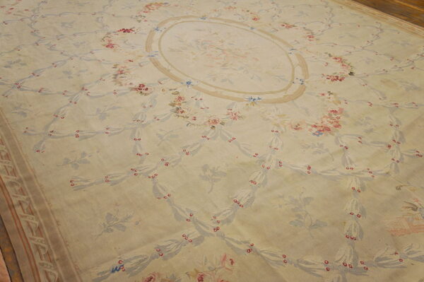 Low-pile cream rug with an ornate pale blue and pink floral trellis pattern on wood flooring.