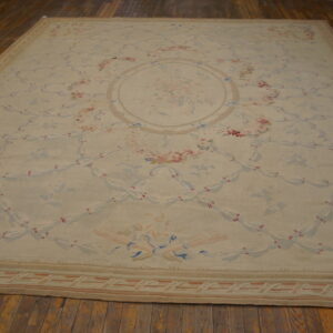 Large cream rug with intricate pink and blue floral and ribbon pattern displayed on a hardwood floor.