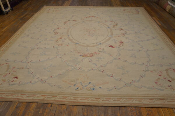 Large cream rug with intricate pink and blue floral and ribbon pattern displayed on a hardwood floor.