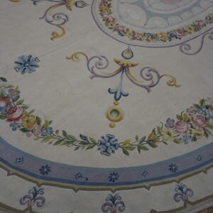 Ornate cream rug with multicolored floral garlands and blue scrolling designs sits on dark wood floors.