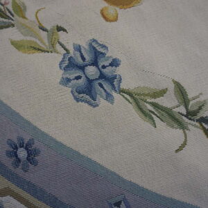 Flat-weave detail showing a large blue flower, green foliage, and a striped mauve border.