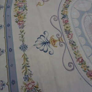 Cream flatwoven rug featuring pastel pink, blue, and yellow floral borders and ornamental scrolls on wood planks.