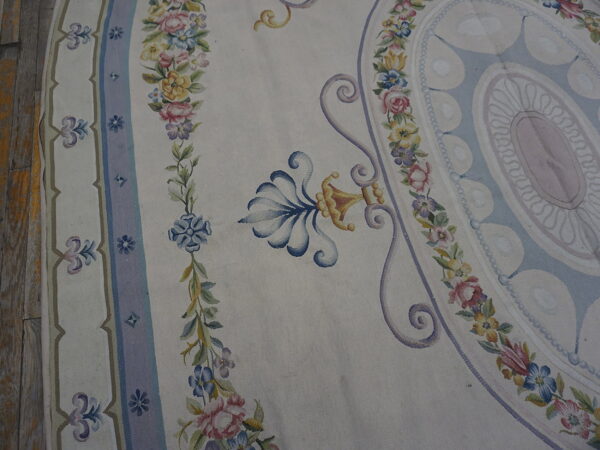 Cream flatwoven rug featuring pastel pink, blue, and yellow floral borders and ornamental scrolls on wood planks.