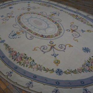 Oval cream rug with detailed blue, pink, and yellow floral patterns resting on rustic wood plank flooring.