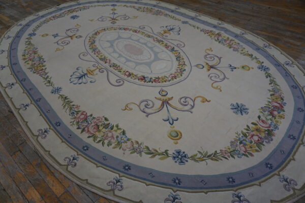 Oval cream rug with detailed blue, pink, and yellow floral patterns resting on rustic wood plank flooring.