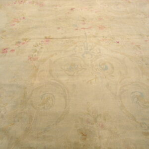 Muted beige rug surface with faint pink floral designs and low-contrast blue classical scrolling patterns.