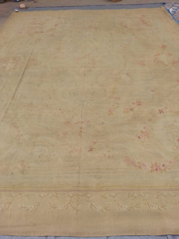 Large pale beige area rug featuring faded pink and cream floral designs on a concrete floor.