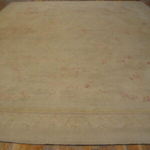Tan low-pile rug with a low-contrast floral pattern and border, displayed on hardwood flooring.