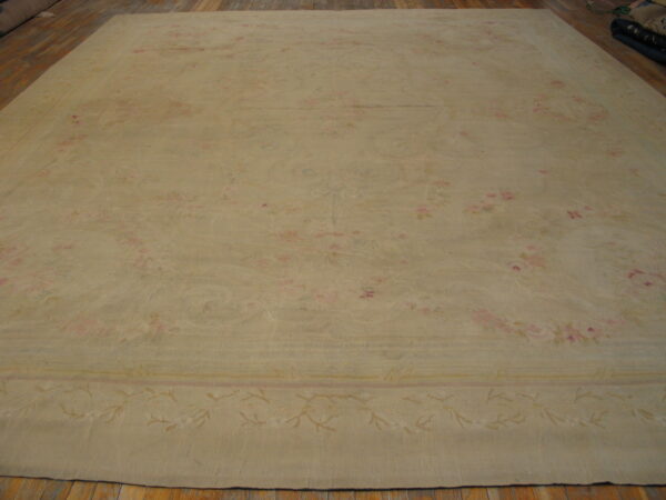 A large pale beige rug with a faint pink and tan floral design lies on hardwood flooring.