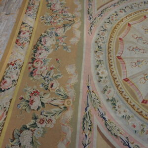 Close-up of a pastel rug featuring floral garlands, pink stripes, and a round medallion on distressed plank flooring.