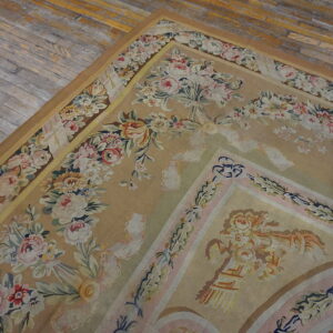 A low-pile tan rug with elaborate pink and cream floral borders lies on distressed grey wooden floors.