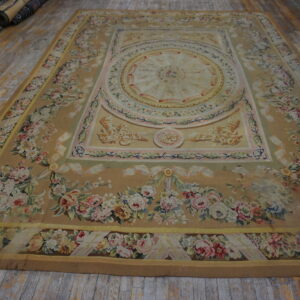 Low-pile beige rug with elaborate pink and cream floral designs displayed on worn plank hardwood flooring.