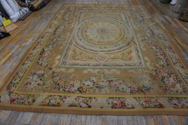 Low-pile beige rug with elaborate pink and cream floral designs displayed on worn plank hardwood flooring.