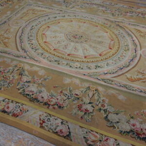 Ornate tan rug featuring a central medallion and pastel pink and cream floral garlands on wood floor.