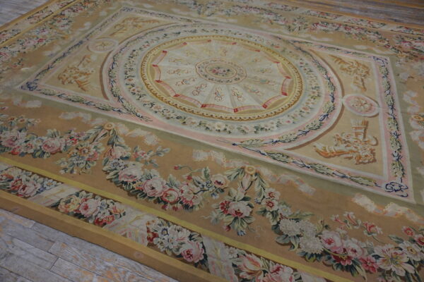 Ornate tan rug featuring a central medallion and pastel pink and cream floral garlands on wood floor.