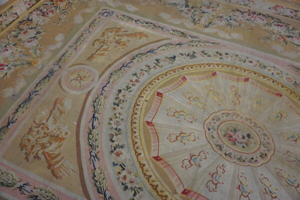 A large rug with an intricate beige, pink, and ivory floral medallion and border design.