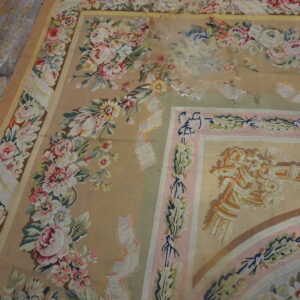 Worn low-pile rug with beige, pink, and green floral tapestry design on weathered wooden planks.
