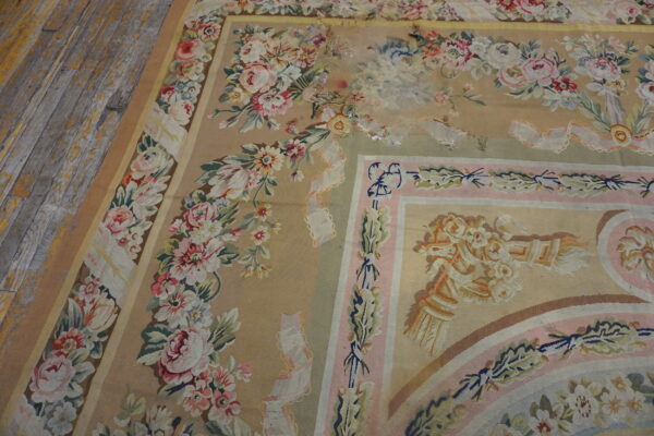 Worn low-pile rug with beige, pink, and green floral tapestry design on weathered wooden planks.