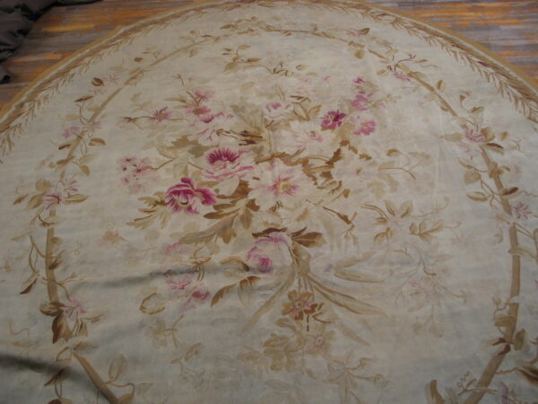 Round cream and pink floral rug featuring large roses and vine patterns on light hardwood flooring.