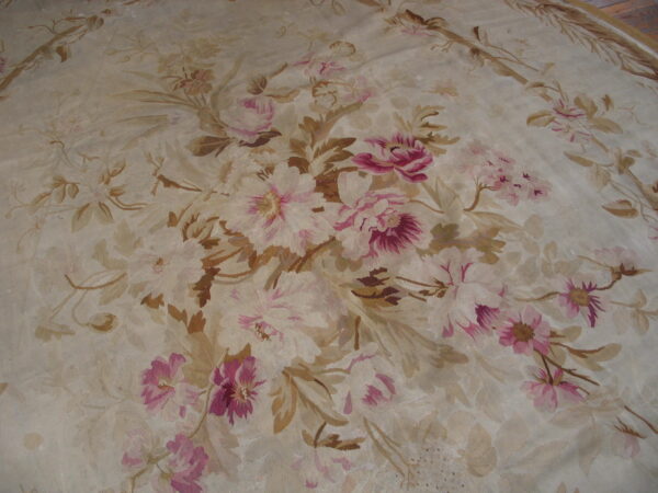 Muted floral rug with rose and magenta blossoms against a low-pile cream and tan woven background.