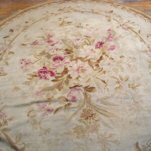 Round low-pile rug with pink and brown floral pattern on a cream background over wood flooring.