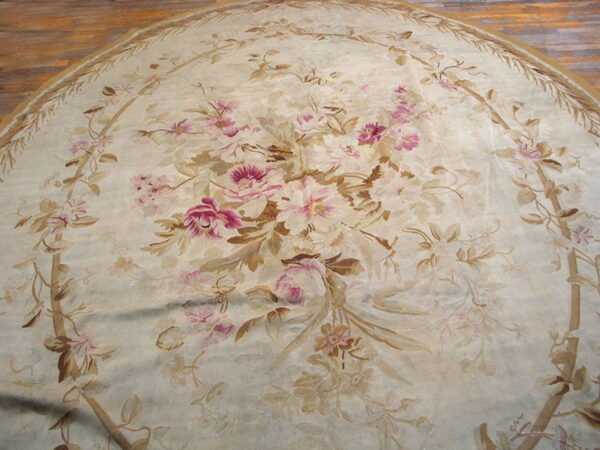 Round low-pile rug with pink and brown floral pattern on a cream background over wood flooring.