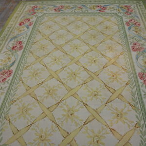 Pale floral rug with yellow trellis pattern and pink rose border lies on gray, distressed hardwood floor.